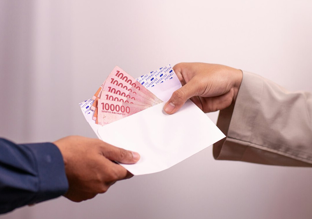 Two hands exchanging a folder of documents across a dark wood table